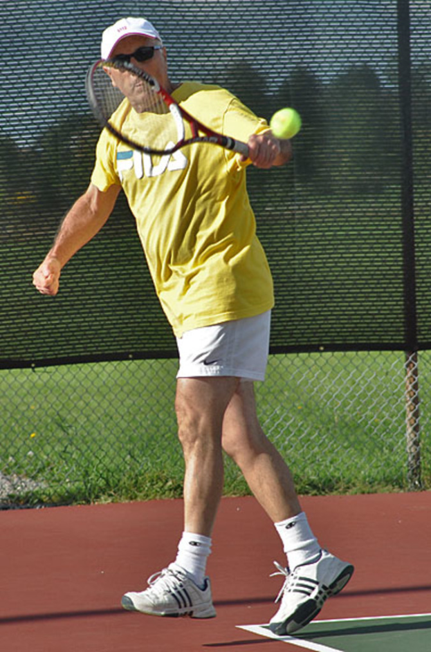 Ein Mann mit Brille, T-Shirt, M√ľtze und Schuhen spielt Tennis.