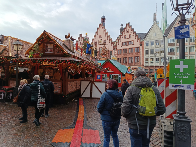 Menschen, die auf einem Kopfsteinpflasterweg neben einem Weihnachtsmarkt in Nürnberg, Deutschland, gehen, mit Laternenmasten und Texttafeln im Vordergrund und Gebäuden im Hintergrund und einem bewölkten Himmel.