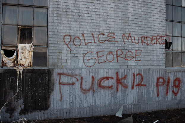 Graffiti an einer Hauswand mit der Aufschrift "Polizei mordet George Fuck 12 P19" mit Fenstern und verstreuten Gegenständen davor.