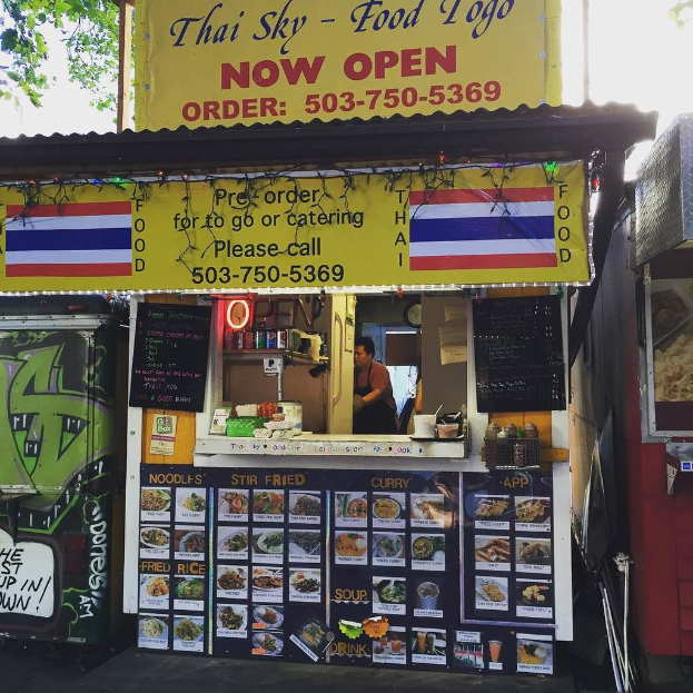 Ein Geschäftsvorplatz mit verschiedenen Artikeln wie Getränkedosen, Speisekarten, einer Uhr, Gewürzen in Plastikbehältern, Gewürzen, Werbetafeln und Namensschildern unter einem Himmel.