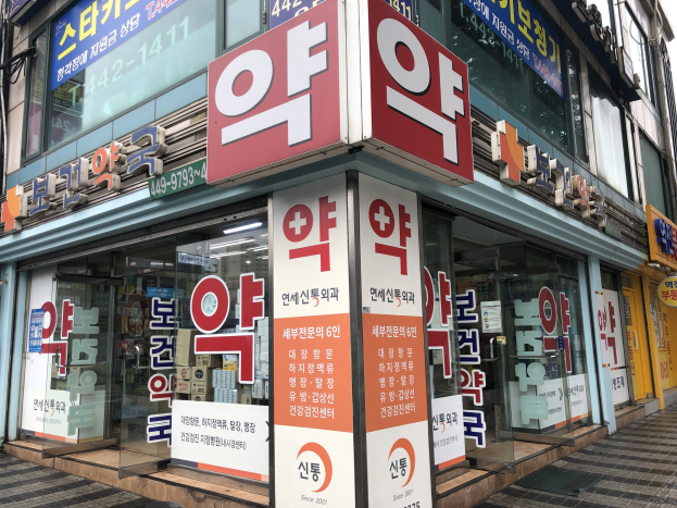 Außenansicht eines modernen Gebäudes mit Glaswänden und -türen, das ein Schild und Schilder trägt, die "Südkoreas erste Apotheke in Seoul, Südkorea" anzeigen.