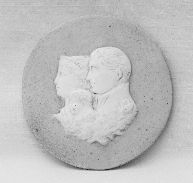 Ein Schwarz-Weiß-Foto eines Mannes in einem Anzug, der ein Baby hält, neben einer Frau, alle im Profil vor einem unscharfen Hintergrund.