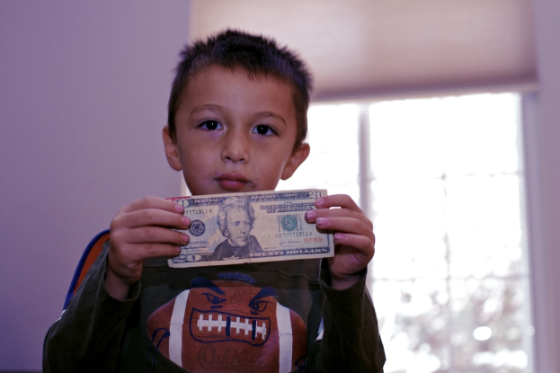 Ein Junge steht mit Geld in der Hand vor einem Fenster und einer Wand.