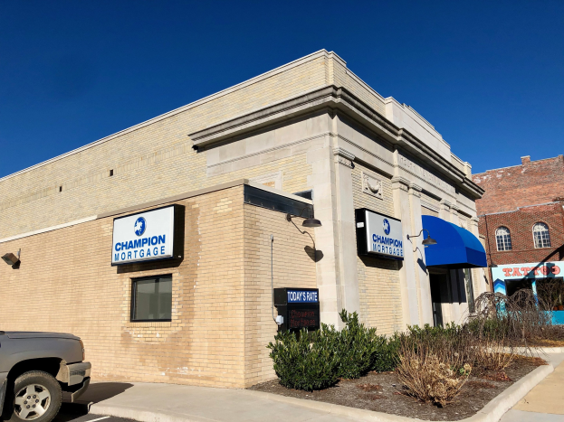 Ein zweistöckiges Gebäude mit vernagelten Fenstern, einem geparkten Auto und Topfpflanzen davor, die "Champion Mortgage, Inc."-Schilder tragen, mit Bäumen und einem bewölkten Himmel im Hintergrund.