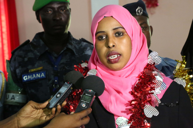 Eine Frau mit pinkem Kopftuch spricht zu Reportern während eines Interviews, wobei ein Mikrofon auf der linken Seite und eine abgehängte Wand im Hintergrund zu sehen sind.