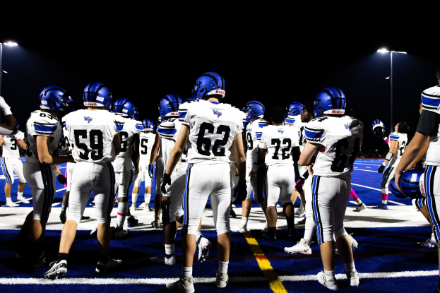Eine Gruppe von Fussballspielern in Helmen und Stiefeln steht auf einem Feld, mit Leuchtmasten im Hintergrund.