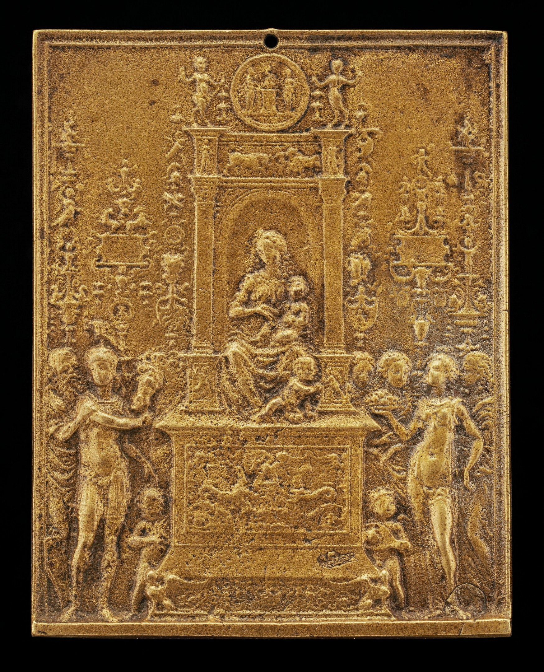 Goldene Plakette mit detaillierter Skulptur einer Frau in einem wallenden Kleid und eines Mannes in Anzug und Krawatte vor schwarzem Hintergrund, umrahmt von einem goldenen Rahmen.