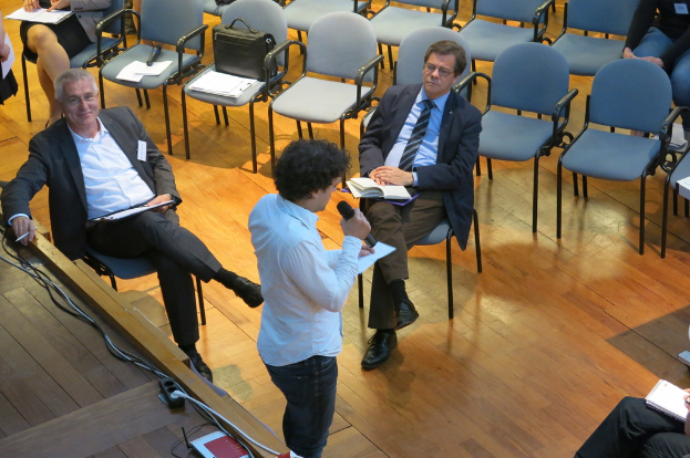 Eine Gruppe von Menschen sitzt mit Büchern und hört aufmerksam einem Redner mit Mikrofon zu.