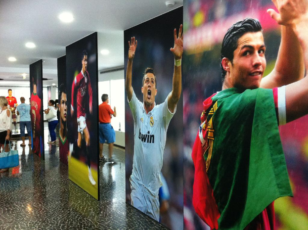 Ein Banner mit dem Fußballspieler Rolando, auf dem Menschen links neben einem Tisch stehen und Lichter oben zu sehen sind.