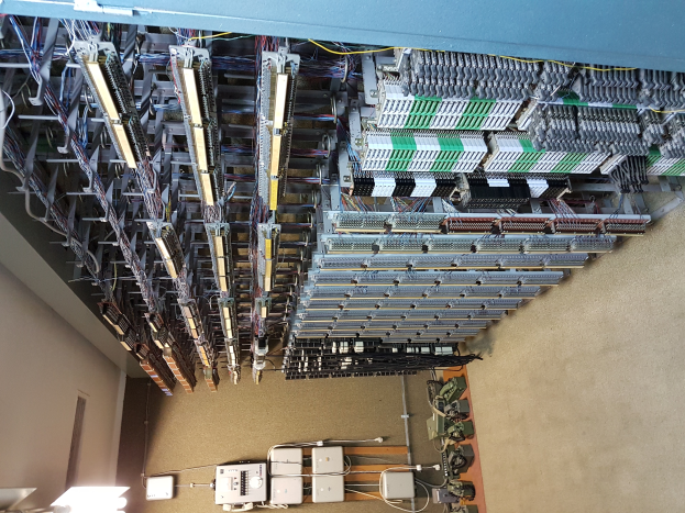 Ein geräumiger Raum voller Numerous Wires und elektronische Geräte auf dem Boden, mit einer Wand auf der linken Seite, scheint ein Datenzentrum mit verschiedenen Servern und miteinander verbundenen Kabeln zu sein.