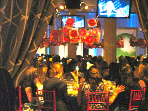 Eine Gruppe von Menschen an Tischen mit Essen, Fernsehern, hängenden Papieren und Vorhängen in einem Raum mit Lichtern.