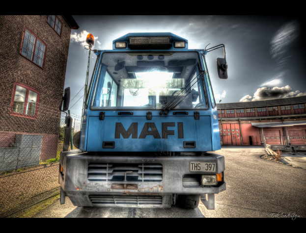 Eine animierte Abbildung eines Busses mit Nummernschild, einem Gebäude mit Fenstern auf der linken Seite, einem Wasserzeichen in der rechten Ecke und einem Hintergrund mit einem weiteren Gebäude und einem bewölkten Himmel.