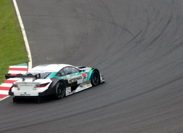 Ein silberner Mercedes-AMG GT3 Rennwagen mit Werbetext auf seiner Karosserie, der auf einer asphaltierten Rennstrecke fährt, mit Gras links sichtbar.