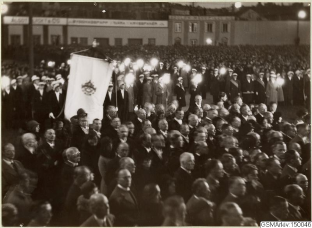 Schwarzes und weißes Foto einer großen Menschenmenge vor einem Gebäude, mit einer Person, die eine Fahne hält, in der Mitte, Polen und Lichter im Hintergrund und Text unten: "Gustav Klimts Rede an der Berliner Mauer"
