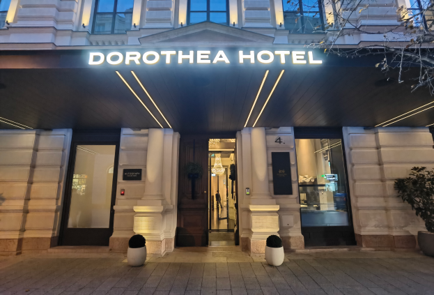 Das Dorothea Hotel in London, England, ein Gebäude mit Glasfenstern und -türen, ein Namensschild, Topfpflanzen, ein Baum und Deckenleuchten unter einem Dach.