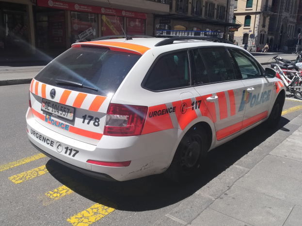 Ein weißer und oranger Polizeiwagen auf einer Straße geparkt, mit Fahrrädern auf dem benachbarten Gehweg und Passanten im Hintergrund.
