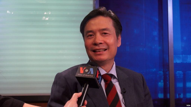 Ein Mann im Anzug mit Mikrofon, mit der Hand eines Reporters sichtbar, der während eines Interviews spricht