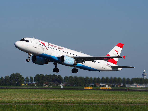 Ein Airbus A320-200 der Austrian Airlines startet vom Frankfurter Flughafen, mit grünem Gras, Bäumen, Gebäuden und einem Tower im Hintergrund.