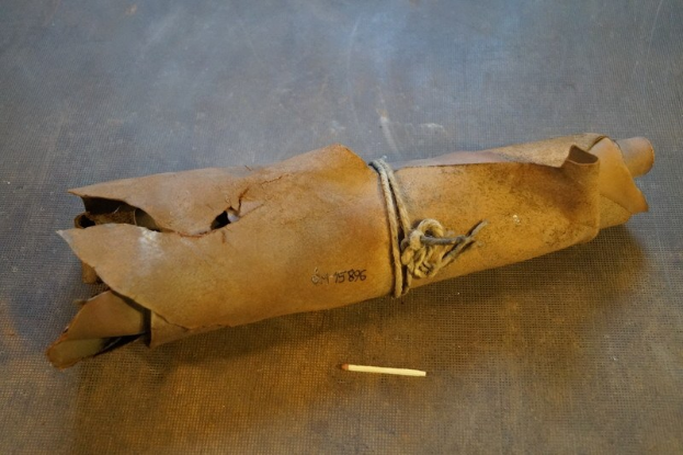 Eine braune Papiertüte, die wie eine Granate aussieht, mit einem Seil verschnürt und auf einem Tisch platziert, mit einer Zigarette daneben.