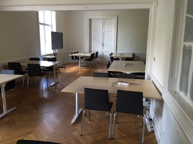 Großer Konferenzraum in Paris mit Tischen, Stühlen, einem Fernseher, einer Tür, einem Fenster und einer Wand.