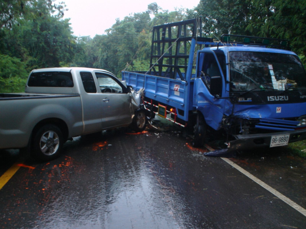 Ein Truck mit eingedrückter Front und verbeulter Karosserie auf der Seite einer Straße stehend, umgeben von Bäumen unter einem klaren blauen Himmel.