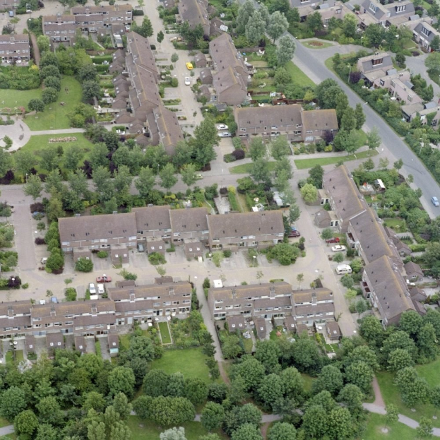 Luftaufnahme eines Wohnviertels mit Häusern, Bäumen, Gras, Straßen und Fahrzeugen.