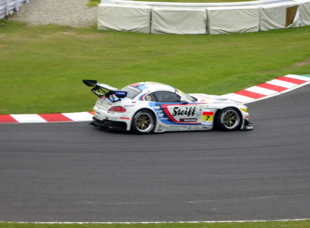 Ein Porsche 911 GT3 RSR-Rennwagen auf einer Rennstrecke, umgeben von grünem Gras und einem Zaun, mit Text und Zahlen, die seine Teilnahme an den 24 Stunden von Le Mans anzeigen.