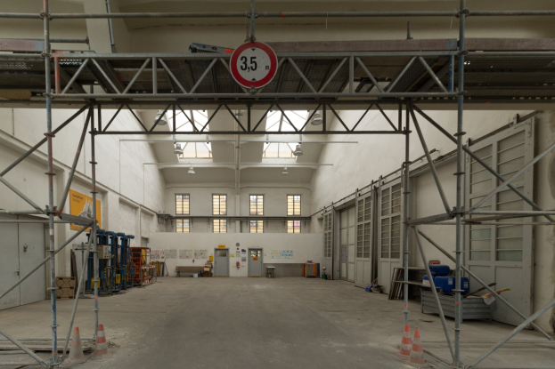 Großes Lagerhaus im Bau mit Gerüsten, Verkehrszeichen, Metallstangen, einem Schild, Maschinen, einer Tür, Fenstern, Wänden, Deckenleuchten und einem Dach.