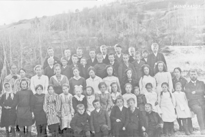 Ein Schwarz-Weiß-Foto einer Gruppe von Kindern, die vor Bäumen und einem Hügel posen, mit dem Text "1930-1940 Schulkinder" unten.