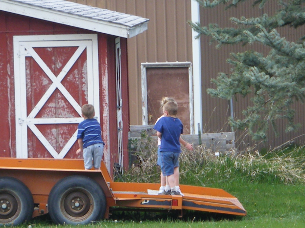 Ein Wagen mit Kindern darauf steht im Zentrum einer grünen Fläche, mit einem Baum und einem Haus im Hintergrund.