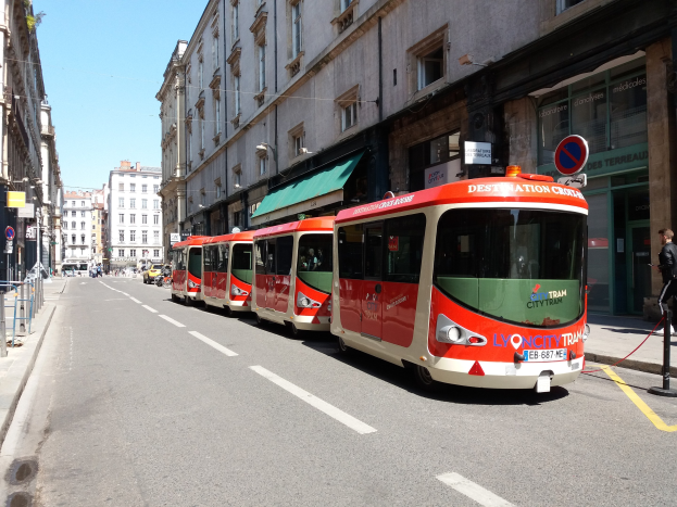Eine Reihe roter und weißer Busse, die entlang einer Straße in Lyon, Frankreich, geparkt sind, mit Passanten auf dem benachbarten Gehweg und Gebäuden, die die Straße säumen.