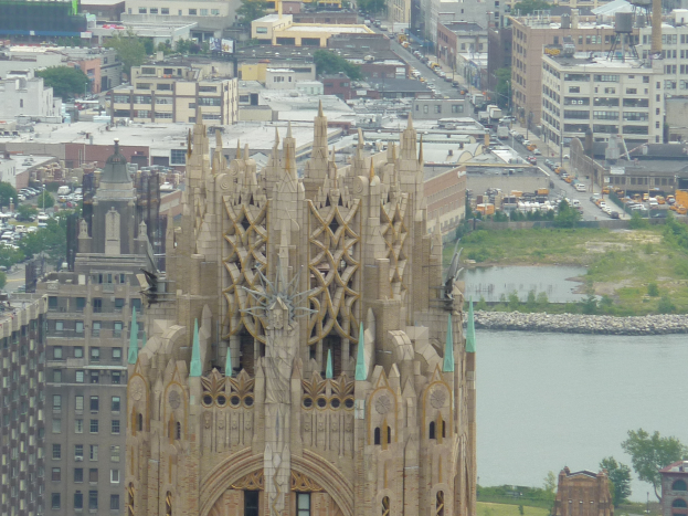 Eine Stadtansicht von einem hohen Aussichtspunkt, die die Sagrada Familia in Barcelona, Spanien, mit zahlreichen Gebäuden, Bäumen, Fahrzeugen und Wasser im Vordergrund zeigt.