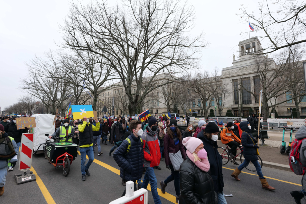 Eine große Protestdemo in Washington, D.C. am 21. Januar 2020, mit Menschen, die spazieren gehen, Schilder halten und Fahrräder fahren, vor einem Gebäude auf einer klaren blauen Straße.