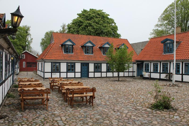 Headsteinstraße mit Außensitzgelegenheiten vor einem Gebäude in Heidelbergs Altstad, umgeben von Grün, einem Laternenmast und einem klaren blauen Himmel.