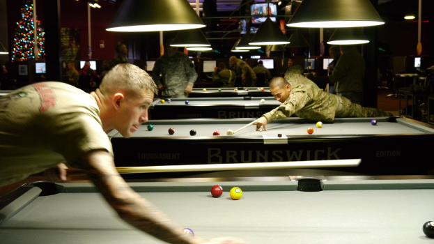 Ein Raum mit Snookertischen, Spielern auf beiden Seiten, hängenden Lampen, einem Weihnachtsbaum in einer Ecke und Bildschirmen mit Ergebnissen.