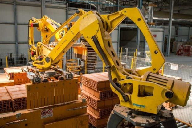 Großes Industriegelände mit gestapelten Kisten, Kränen, Zaun, Pfählen und einer fernen Wand in einer automatisierten Fertigungsumgebung.