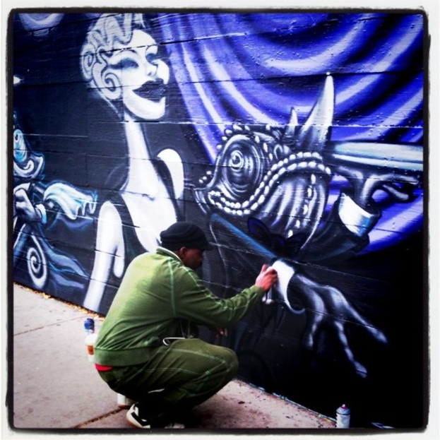 Eine Person hält eine Flasche in der Hand und steht auf einer Straße, umgeben von mehreren anderen Flaschen, mit einer graffitibeschmierten Wand im Hintergrund.