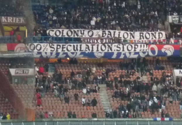 Ein Stadion voller Menschen, Fahnen und Stühle, mit einem Zaun unten und Treppen links.