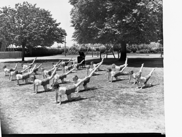 Schwarzes und weißes Foto einer Gruppe von Menschen, die Yoga im Freien in einem Park umgeben von Bäumen und Pflanzen machen.