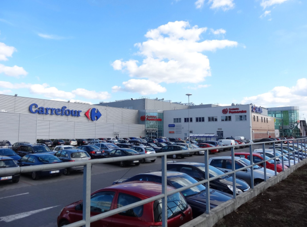Großer Autohandel mit mehreren geparkten Autos, umgeben von Gebäuden, Straßeninfrastruktur und Fahrzeugen auf der Straße.