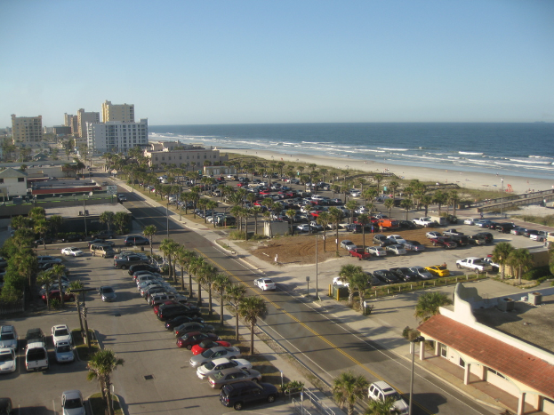Fahrzeuge sind in der Nähe von Bäumen und Gebäuden mit einem Ozean im Hintergrund geparkt.