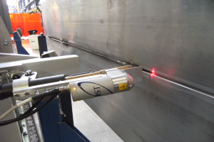 Eine Laser-Schneidmaschine in einer Fabrik strahlt helles Licht aus und erleuchtet die Umgebung mit einer Wand auf der rechten Seite und einigen Gegenständen im Hintergrund.