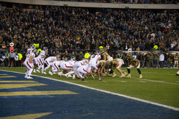 Fußballspieler in Sportkleidung und Helmen liegen auf dem Boden während eines Spiels in einem Stadion mit Zuschauern und Anzeigetafeln im Hintergrund.