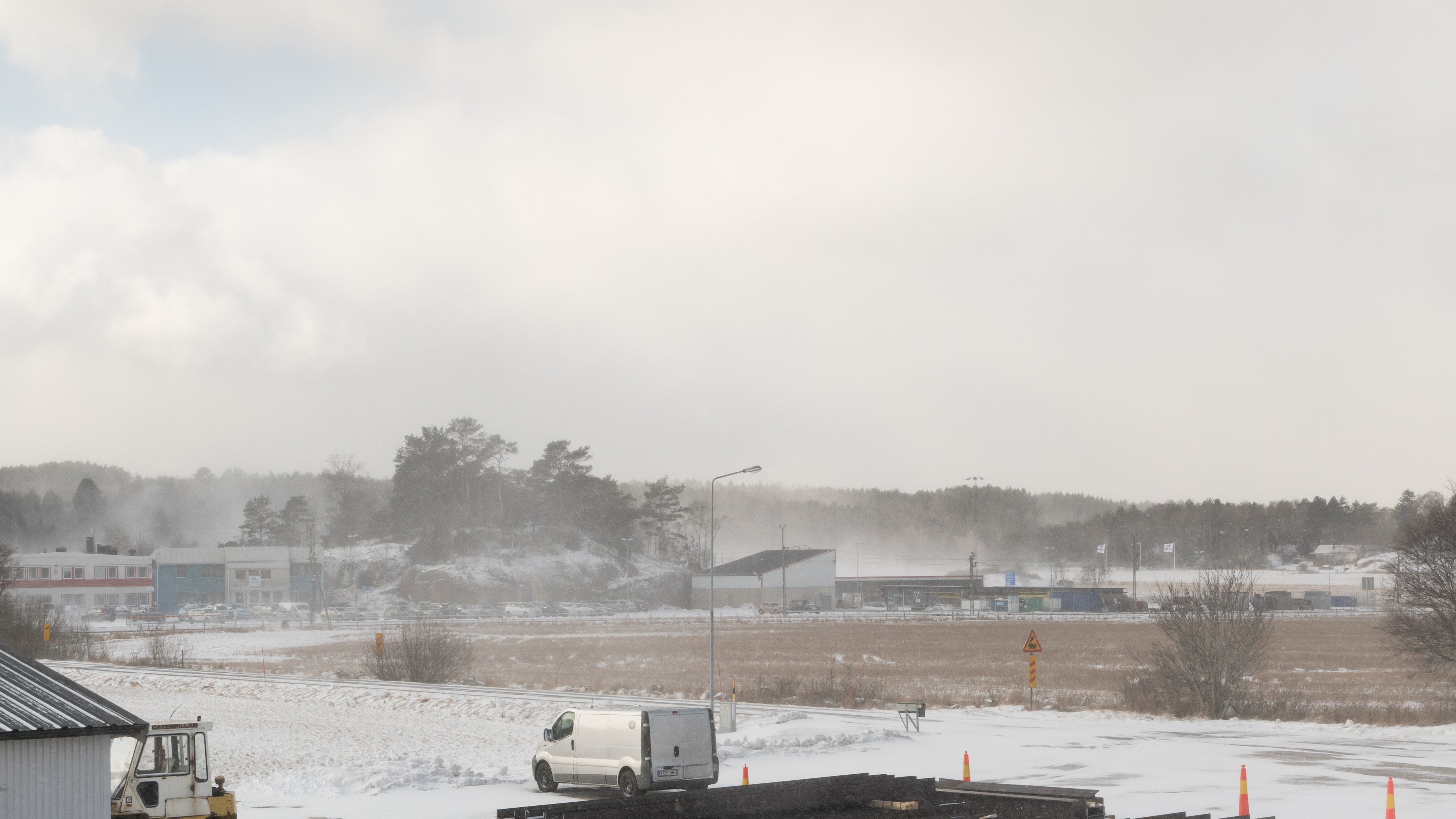 Ein großer Lastwagen parkt tief im Schnee neben einem Gebäude, umgeben von Bäumen, Strommasten, Straßenlaternen und verstreuten Trümmern unter einem bewölkten Himmel.