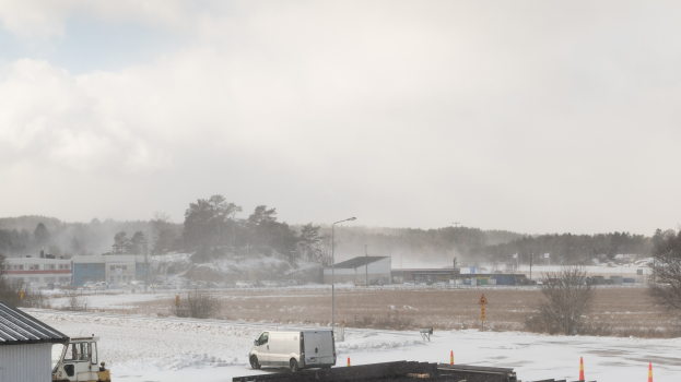Ein großer Lastwagen parkt tief im Schnee neben einem Gebäude, umgeben von Bäumen, Strommasten, Straßenlaternen und verstreuten Trümmern unter einem bewölkten Himmel.