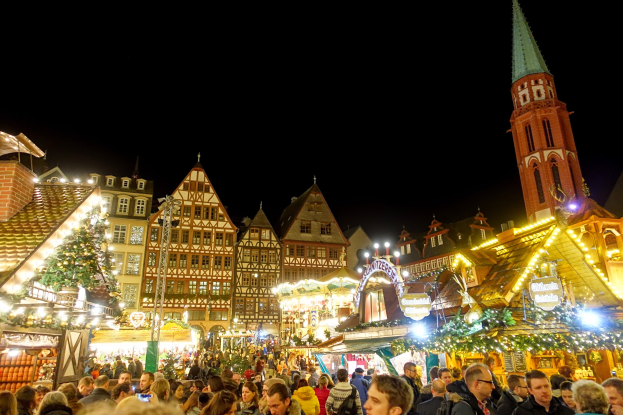Ein geschäftiges Weihnachtsmarkt in Nürnberg, Deutschland mit Menschen um geschmückte Stände, Gebäuden mit Fenstern, einem Uhrenturm und einem dunklen Himmel.