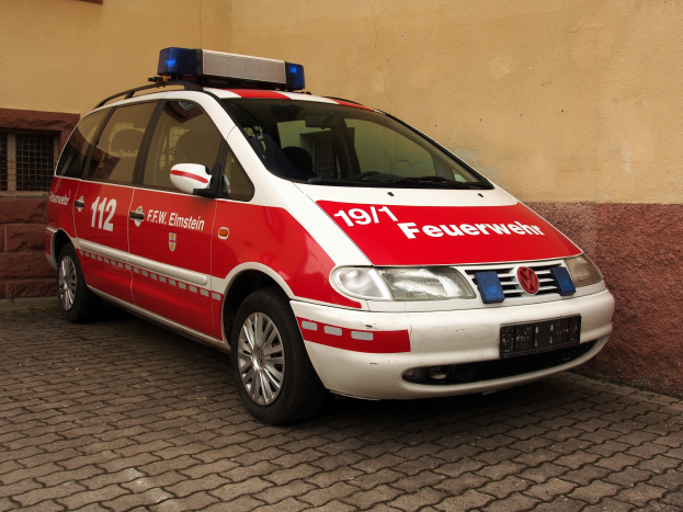 Ein roter und weißer Minivan, der als Krankenwagen gekennzeichnet ist, steht vor einem Fensterfront-Gebäude.