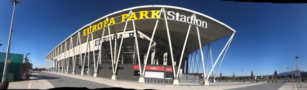 Das Europa-Park-Stadion in Barcelona, Spanien, ein großer Bau mit Text darauf, umgeben von Pfölen, Lichtern, Bäumen und einem Zaun, mit dem Himmel im Hintergrund.