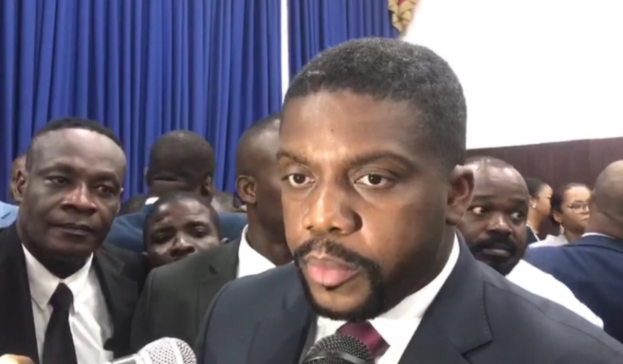 Ein Mann im Anzug und Krawatte spricht vor einem Publikum in ein Mikrofon, mit Vorhängen und einer Wand im Hintergrund, wahrscheinlich in Reaktion auf seine lebenslange Haftstrafe.