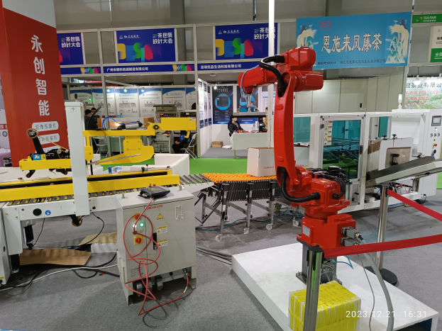 Eine Gruppe von Robotern auf einem Tisch in einer Fabrikumgebung, umgeben von Maschinen, Kabeln und anderen elektronischen Bauteilen sowie ein paar Menschen im Hintergrund.